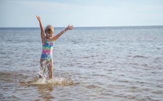 jung glücklich Kind Mädchen von europäisch Aussehen Alter von 6 haben Spaß im Wasser auf das Strand und Spritzwasser, tropisch Sommer- Berufe,Ferien.a Kind genießt das Meer.Familie Ferien konzept.kopie Raum. foto