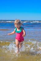 jung glücklich Kind Mädchen von europäisch Aussehen Alter von 4 haben Spaß im Wasser auf das Strand und Spritzwasser, tropisch Sommer- Berufe,Ferien.a Kind genießt das Meer.vertikal Foto. foto