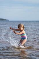 jung glücklich Kind Mädchen von europäisch Aussehen Alter von 6 haben Spaß im Wasser auf das Strand und Spritzwasser, tropisch Sommer- Berufe,Ferien.a Kind genießt das Meer.vertikal Foto. foto