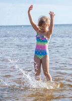 jung glücklich Kind Mädchen von europäisch Aussehen Alter von 6 haben Spaß im Wasser auf das Strand und Spritzwasser, tropisch Sommer- Berufe,Ferien.a Kind genießt das Meer.vertikal Fotokopie Raum. foto