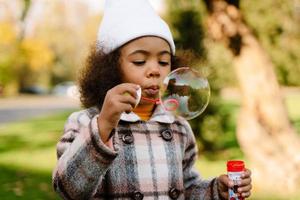 Schwarzes Mädchen bläst Seifenblasen beim Gehen im Herbstpark foto
