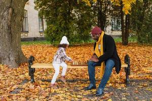 schwarzer Großvater und Enkelin spielen Schach im Herbstpark foto