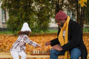 schwarzer Großvater und Enkelin spielen Schach im Herbstpark foto