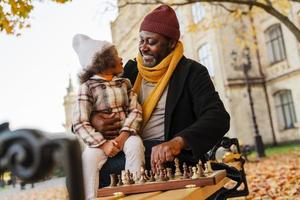 schwarzer Großvater und Enkelin spielen Schach im Herbstpark foto