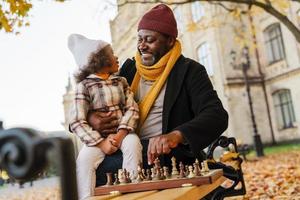 schwarzer Großvater und Enkelin spielen Schach im Herbstpark foto