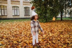 schwarzes Mädchen mit Mantel, das sich mit gefallenen Blättern im Herbstpark lustig macht foto