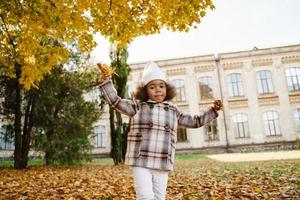 schwarzes Mädchen mit Mantel, das sich mit gefallenen Blättern im Herbstpark lustig macht foto