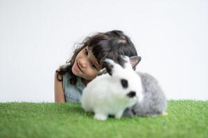 lächelnd wenig Mädchen und mit ihr Geliebte flauschige Kaninchen, präsentieren das Schönheit von Freundschaft zwischen Menschen und Tiere foto