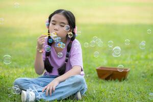 Mädchen Sitzung im das Park mit weht Luft Blase, umgeben durch Grün und Natur foto