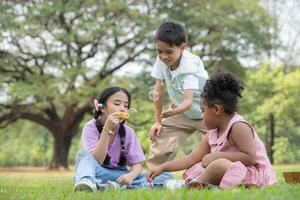 Kinder Sitzung im das Park mit weht Luft Blase, umgeben durch Grün und Natur foto