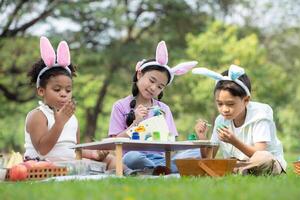 glücklich Familie genießen ein Picknick im das Park, Kinder Sitzung und Färbung ihr schön Ostern Eier. foto