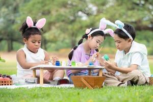 glücklich Familie genießen ein Picknick im das Park, Kinder Sitzung und Färbung ihr schön Ostern Eier. foto