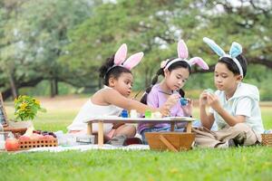 glücklich Familie genießen ein Picknick im das Park, Kinder Sitzung und Färbung ihr schön Ostern Eier. foto