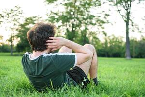 jung Mann mit Grün T-Shirt tun Sit-ups im Park foto