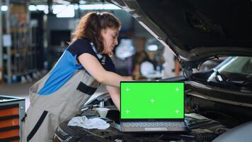 schließen oben Schwenken Schuss von Chroma Schlüssel Laptop im Garage Einrichtung Sitzung auf Fehlfunktion Wagen. Grün Bildschirm Gerät im Reparatur Geschäft Nächster zu Ingenieur Reinigung Teile Innerhalb Fahrzeug foto