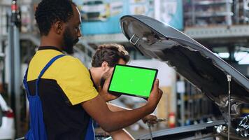 Mechaniker mit Grün Bildschirm Tablette im Auto Bedienung zu Uhr Lernprogramm auf Wie zu Fix Unbekannt Problem. Mitarbeiter mit Chroma Schlüssel Gerät zu aussehen online zum Video zeigen Wie zu Reparatur gebrochen Fahrzeug Teil foto