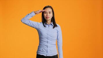 stolz Erwachsene präsentieren Militär- Gruß Symbol im Studio, erziehen Arm Über Tempel und posieren stolz auf Kamera. Filipino Frau salutieren mit Heer Geste gegen Orange Hintergrund. foto