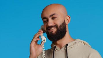 Mitte östlichen Mann reden zu Menschen auf Festnetz Telefon Forderung, antworten retro Maschine Über Blau Hintergrund im Studio. arabisch Person genießen Diskussion mit Kabel Telefon. Kamera 2. foto