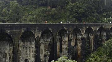 Touristen gehen auf Stein Brücke im Dschungel. Aktion. Menschen gehen auf uralt Stein Brücke im Regenwald. schön Landschaft mit Menschen auf Aquädukt und Grün Hügel foto