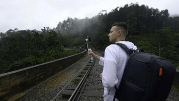 Rückseite Aussicht von ein Mann Tourist nehmen Bilder von Berg bewaldet Landschaft auf Smartphone. Aktion. Wanderer Gehen auf Eisenbahnen. foto