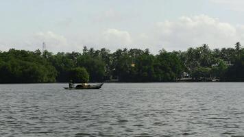 Fischer im ein Boot Segeln im breit Fluss. Aktion. klein Boot und Grün bewaldet Ufer. foto