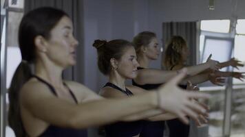 entspannt Sport Mannschaft Stehen während Gruppe Ausbildung im geräumig Studio. Medien. Frauen Atem tief und schwingen ihr Hände, Konzept von Yoga und Entspannung. foto
