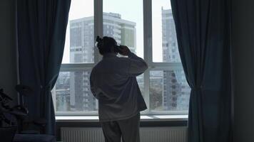 Rückseite Aussicht von ein Frau reden auf ein Zelle Telefon durch das Fenster. Medien. Frau im Pyjama reden auf Smartphone beim heim. foto