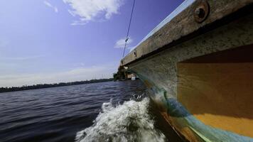 Angeln Boot im das Fluss, zuerst Person Sicht. Aktion. alt Boot schwebend entlang Grün Ufer und Blau wolkig Himmel auf das Hintergrund. foto