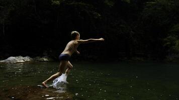 Junge Kind Springen im kalt Berg Fluss auf ein Sommer- Tag. kreativ. Wandern im Sommer- Dschungel. foto