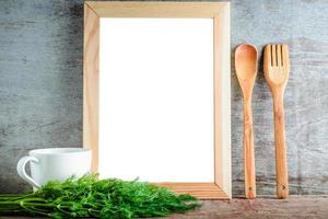 leerer Holzrahmen mit isoliertem weißem Hintergrund und Küchenutensilien und grünem Dill auf Holzuntergrund foto