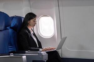 asiatisch jung Frau mit Laptop beim zuerst Klasse auf Flugzeug während Flug, Reisen und Geschäft Konzept foto