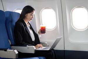 asiatisch jung Frau mit Laptop während Trinken Kaffee beim zuerst Klasse auf Flugzeug während Flug, Reisen und Geschäft Konzept foto