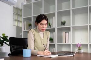 Frau asiatisch kreativ im Zuhause Büro und Laptop zum Forschung im Fernbedienung arbeiten, Sozial Medien oder Blog im Wohnung. freiberuflich beim Schreibtisch mit Computer Schreiben Email, Webseite Post und online Plaudern im Haus foto