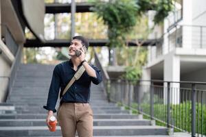 lächelnd asiatisch Geschäftsmann Gehen zu Arbeit während zu halt wiederverwendbar Öko freundlich ökologisch Tasse im das Stadt foto