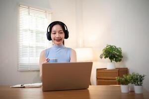 glücklich jung Frau asiatisch im Kopfhörer und Laptop Herstellung Anmerkungen, Mädchen Schüler reden durch Video Konferenz Forderung, online Ausbildung foto