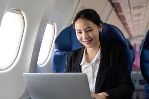 asiatisch jung Frau mit Laptop beim zuerst Klasse auf Flugzeug während Flug, Reisen und Geschäft Konzept foto