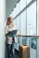 glücklich jung Frau asiatisch ist Stand im Flughafen in der Nähe von Koffer und lesen Karte foto