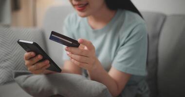 selektiv Fokus, Hände von jung asiatisch Frau Sitzung auf Sofa halten Anerkennung Karte Herstellung online Zahlung zum Kauf im Netz Geschäft mit Smartphone. foto