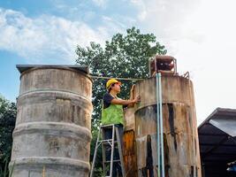 ingenieur, der die qualität des wassers kontrolliert, steht auf den riskanten treppen an hohen orten, die industrielle wasserreinigungs- oder filtrationsanlagen betreiben, alte zementtanks, um wasser in der wasserfabrik zu halten foto