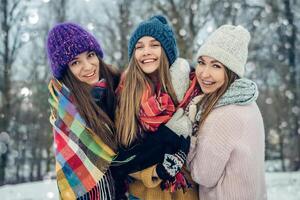 drei Frauen freunde draußen im gestrickt Hüte haben Spaß auf ein schneebedeckt kalt Wetter. Gruppe von jung weiblich freunde draußen im Winter Park. foto
