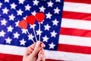 drei rot Herzen gestalten auf Stock im Vorderseite von amerikanisch Flagge. visuell Konzept von Vorbereitung zum Unabhängigkeit Tag. vierte von Juli patriotisch Konzept. foto
