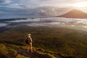 Mann Tourist sieht aus beim das Sonnenaufgang auf das Vulkan batur auf das Insel von bla im Indonesien. Wanderer Mann mit Rucksack Reise auf oben Vulkan, Reise Konzept foto