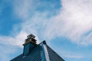 Rauch steigt an von ein Kamin auf das Grün gewellt Dach von ein Haus gegen das Blau Himmel foto