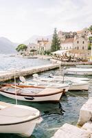 Reihe von Angeln Boote festgemacht beim das perast Seebrücke gegen das Hintergrund von uralt Stein Häuser beim das Fuß von das Berge. Montenegro foto