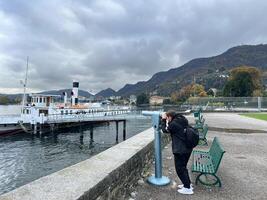 komm, Italien - - 12 November 2023. Mann sieht aus durch ein Teleskop beim das Meer Stehen auf das Ufer beim das Fuß von das Berge foto
