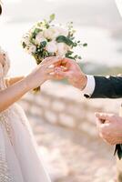 Bräutigam setzt ein Ring auf das Finger von Braut mit ein Strauß von Blumen. abgeschnitten. gesichtslos foto