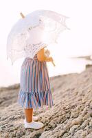 wenig Mädchen mit ein Weiß durchbrochen Sonne Regenschirm steht auf das Strand foto
