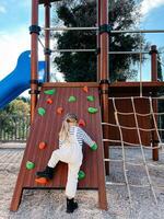 wenig Mädchen klettert das Klettern Mauer im das Spielplatz. zurück Aussicht foto