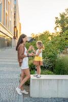 Mama und ihr wenig Tochter spielen auf Stadt Straße im Sonnenuntergang Zeit. hoch Qualität Foto