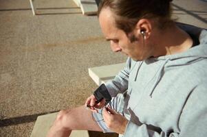 selektiv Fokus auf ein Sportler halten Kopfhörer und Smartphone, entspannend nach draußen trainieren foto